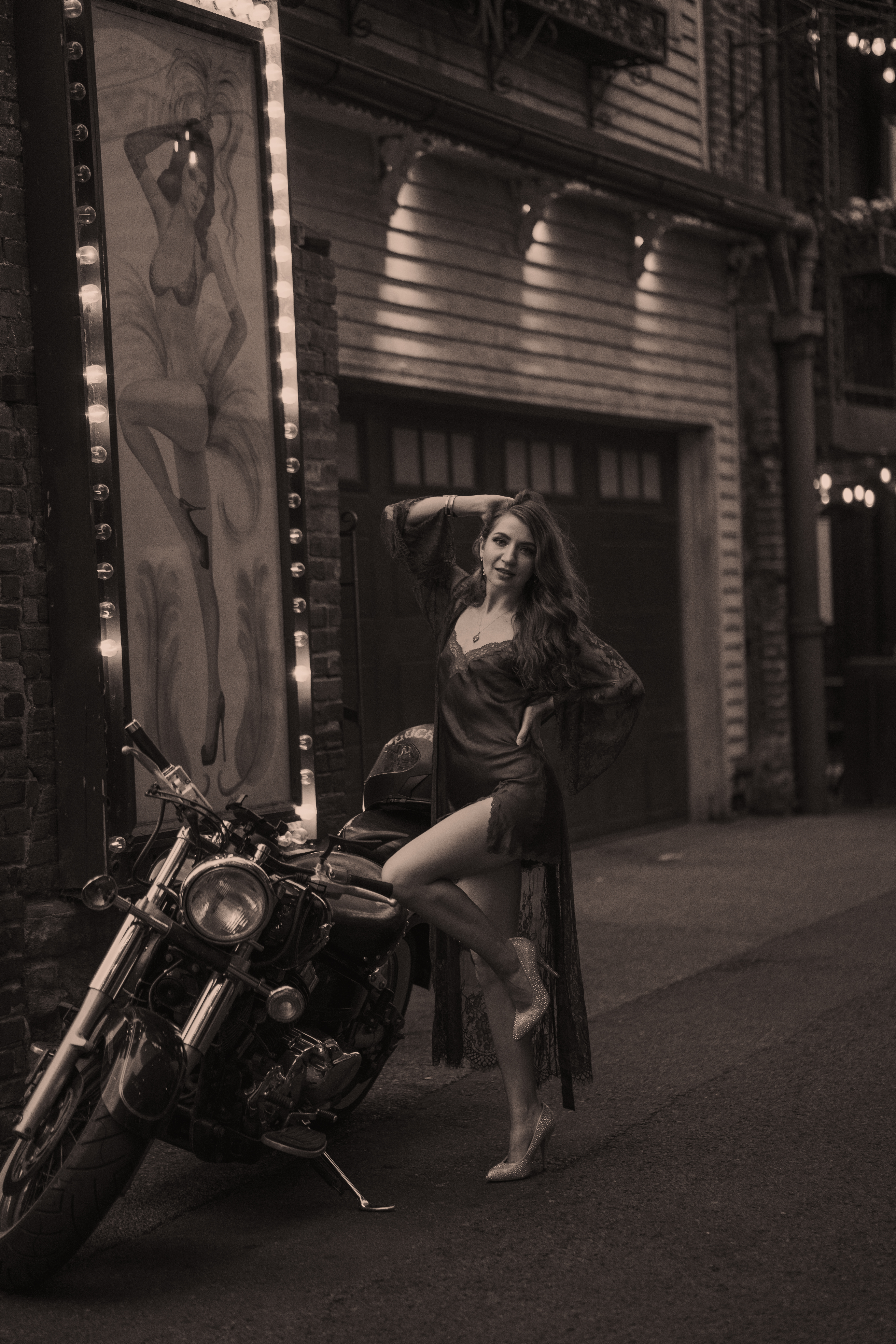 Nashville jazz singer poses in front of motorcycle in a short silk dress with a feathered dancer behind her in Printer's Alley.