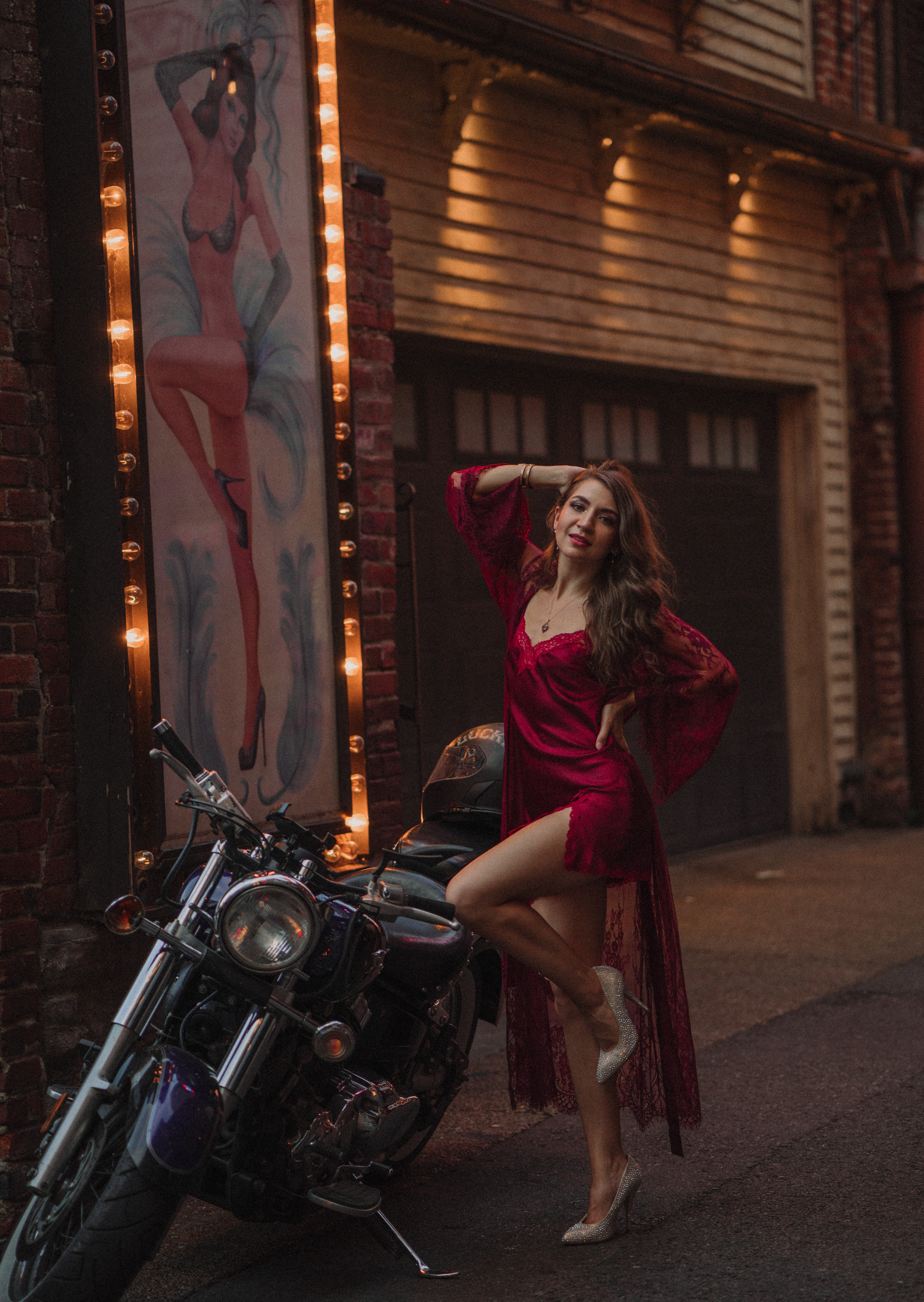 Nashville jazz singer poses in front of motorcycle in a short silk dress with a feathered dancer behind her in Printer's Alley.