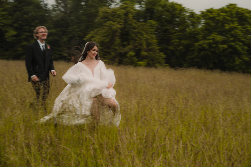 Man and woman running through a field in wedding clothes with a storm brewing in the background.