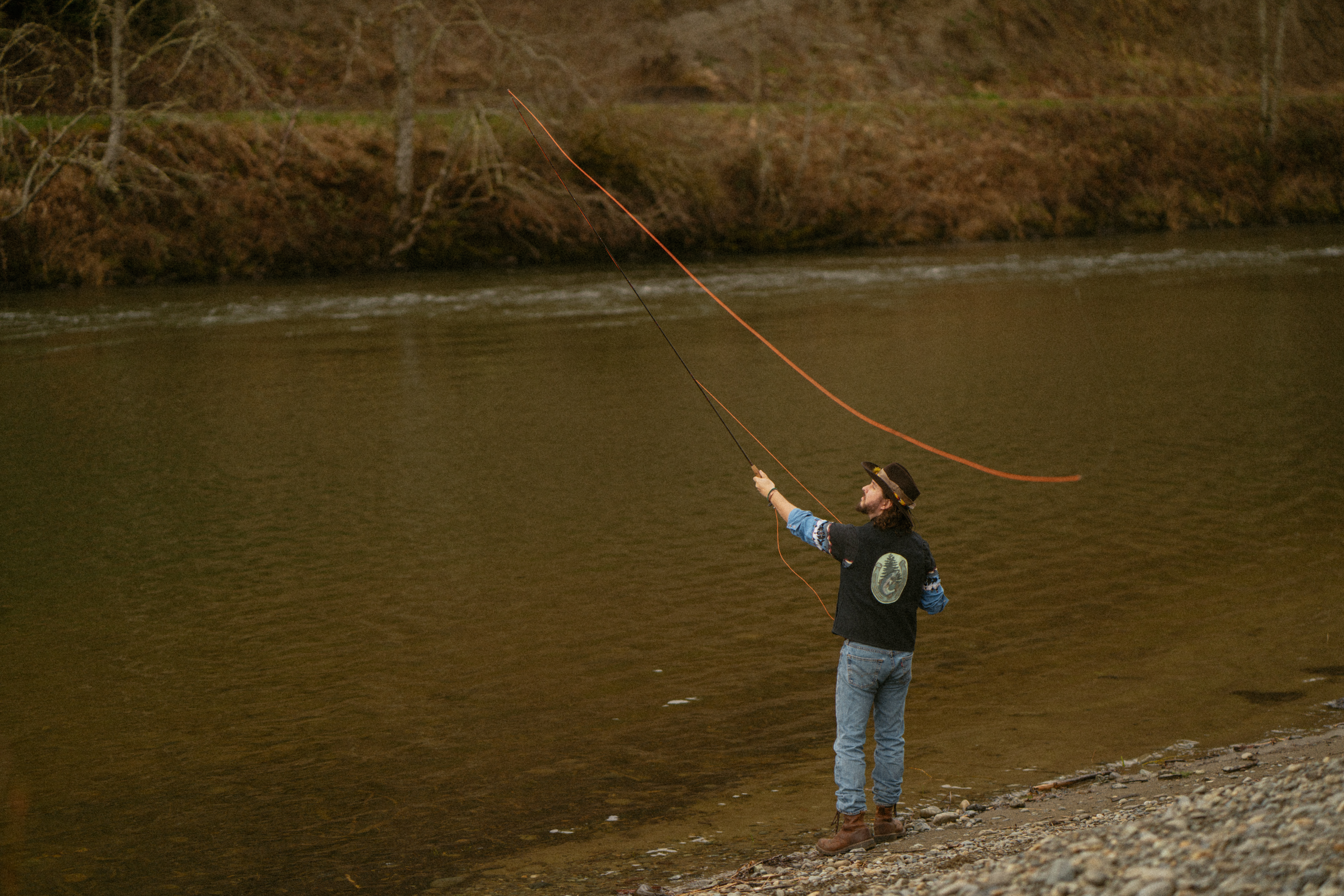 Country musician in cowboy hat casts flyfishing pole into river in Washington